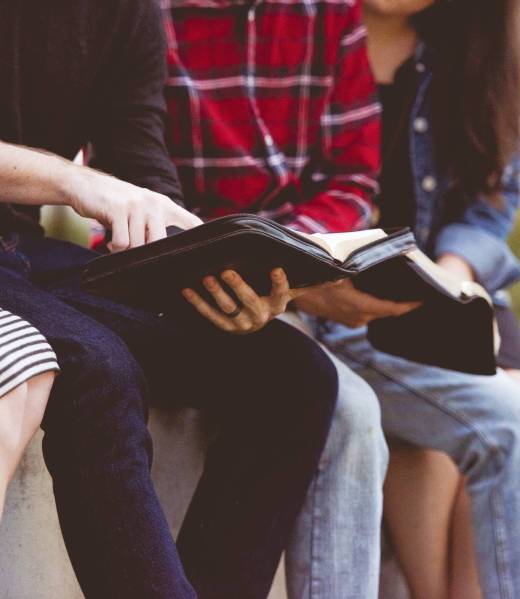 A closeup shot of a person pointing out a line in the bible to females with a blurred background