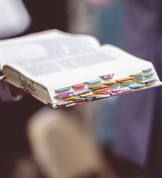 A hand holding an open Bible book with bookmarks